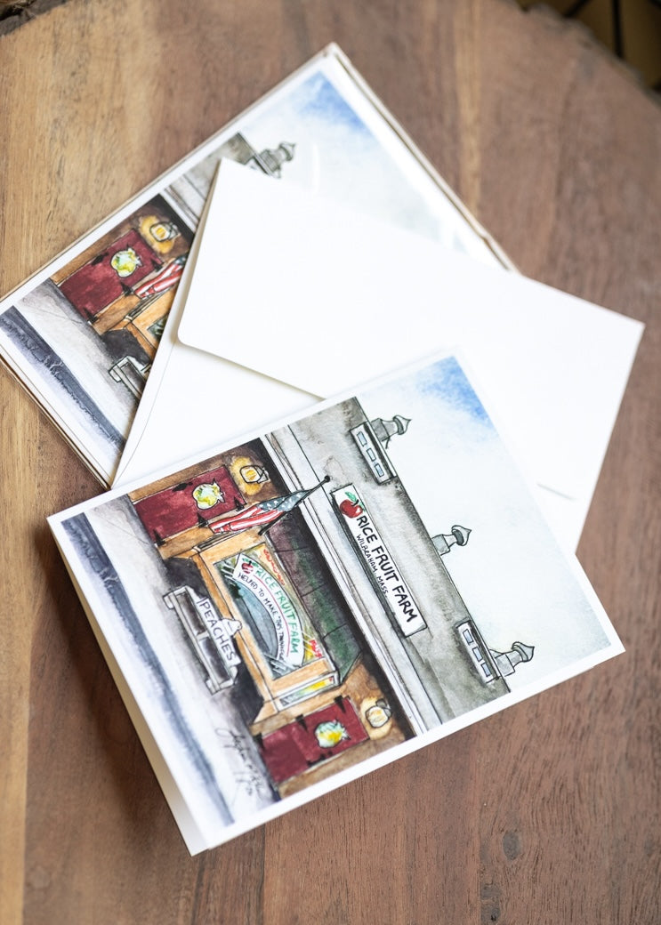 A set of illustrated postcards and white envelopes arranged on a wooden tabletop. The postcards feature watercolor-style drawings of storefronts and street scenes.