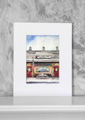 A watercolor art print of the 'Peach Fruit Stand' in wilbraham, ma, displayed on a white surface against a textured gray background.